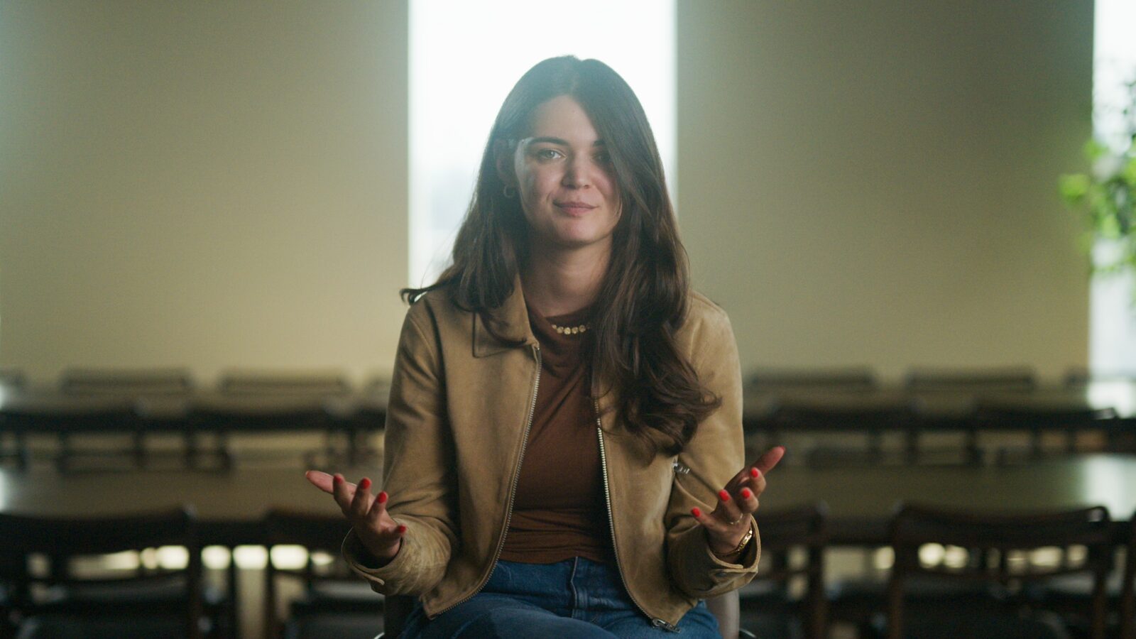 A founder in a tan jacket, hands open in a shrug.